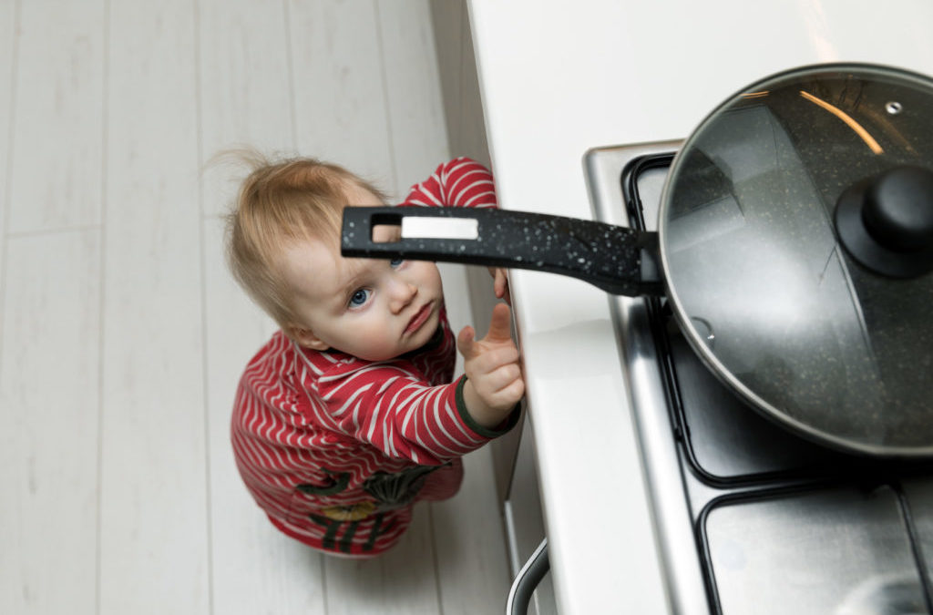 Kindersichere Küche: Ein Kleinkind versucht, an eine Bratpfanne heranzukommen, die auf dem Herd steht