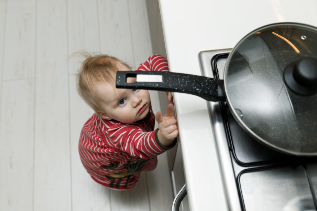 Kindersichere Küche: Ein Kleinkind versucht, an eine Bratpfanne heranzukommen, die auf dem Herd steht