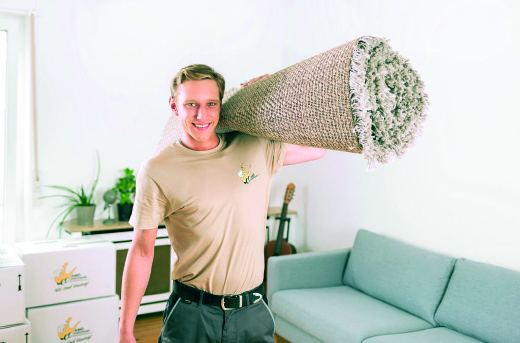 Ein Facharbeiter trägt einen zusammengerollten Teppich (Wohnungswechsel).