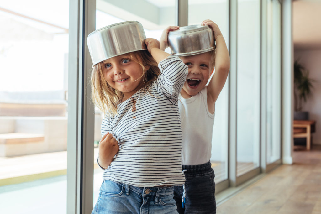 Zwei kleine Kinder haben einen Topf auf dem Kopf und lachen (laute Nachbarn).