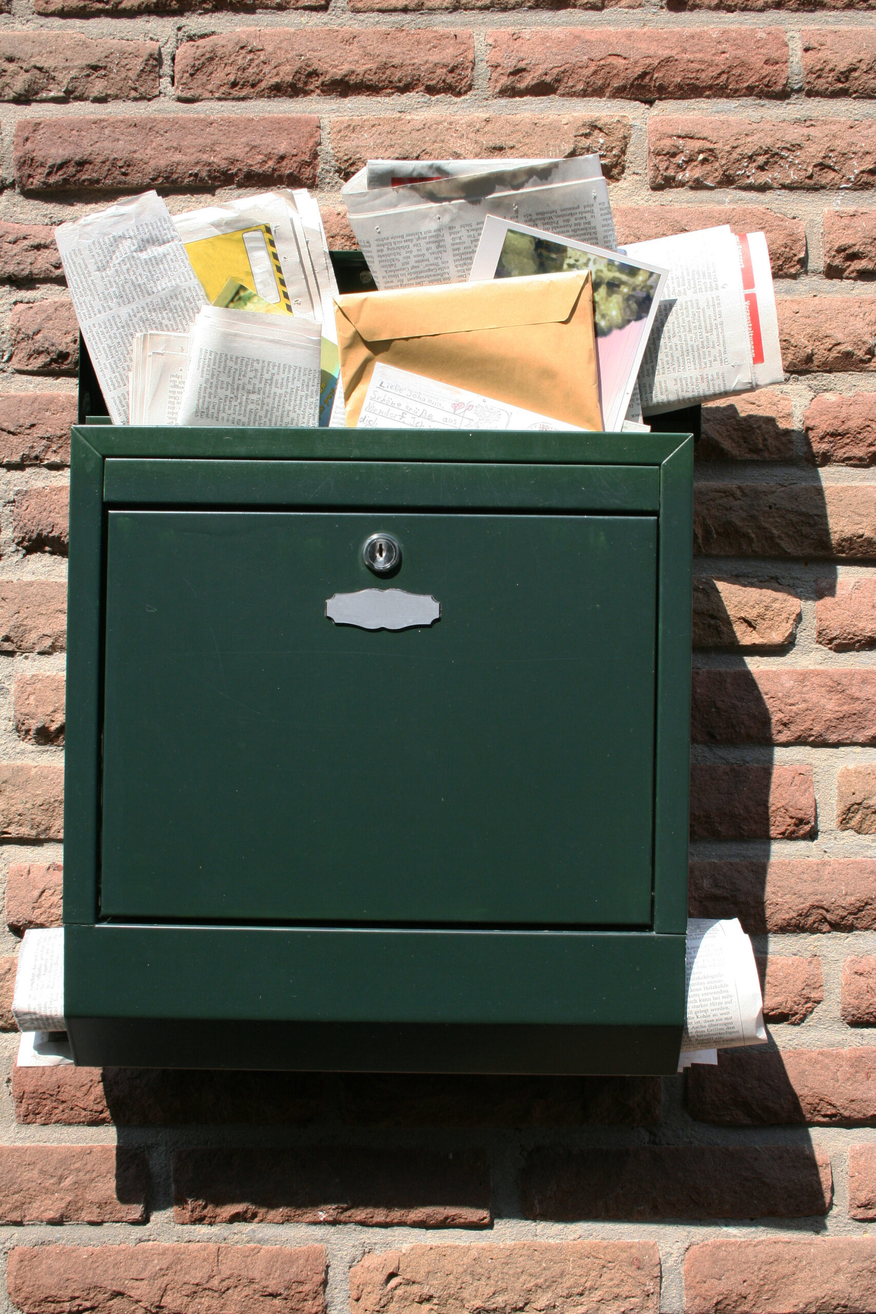 Grüner überfüllter Briefkasten an der Wand eines Hauses.