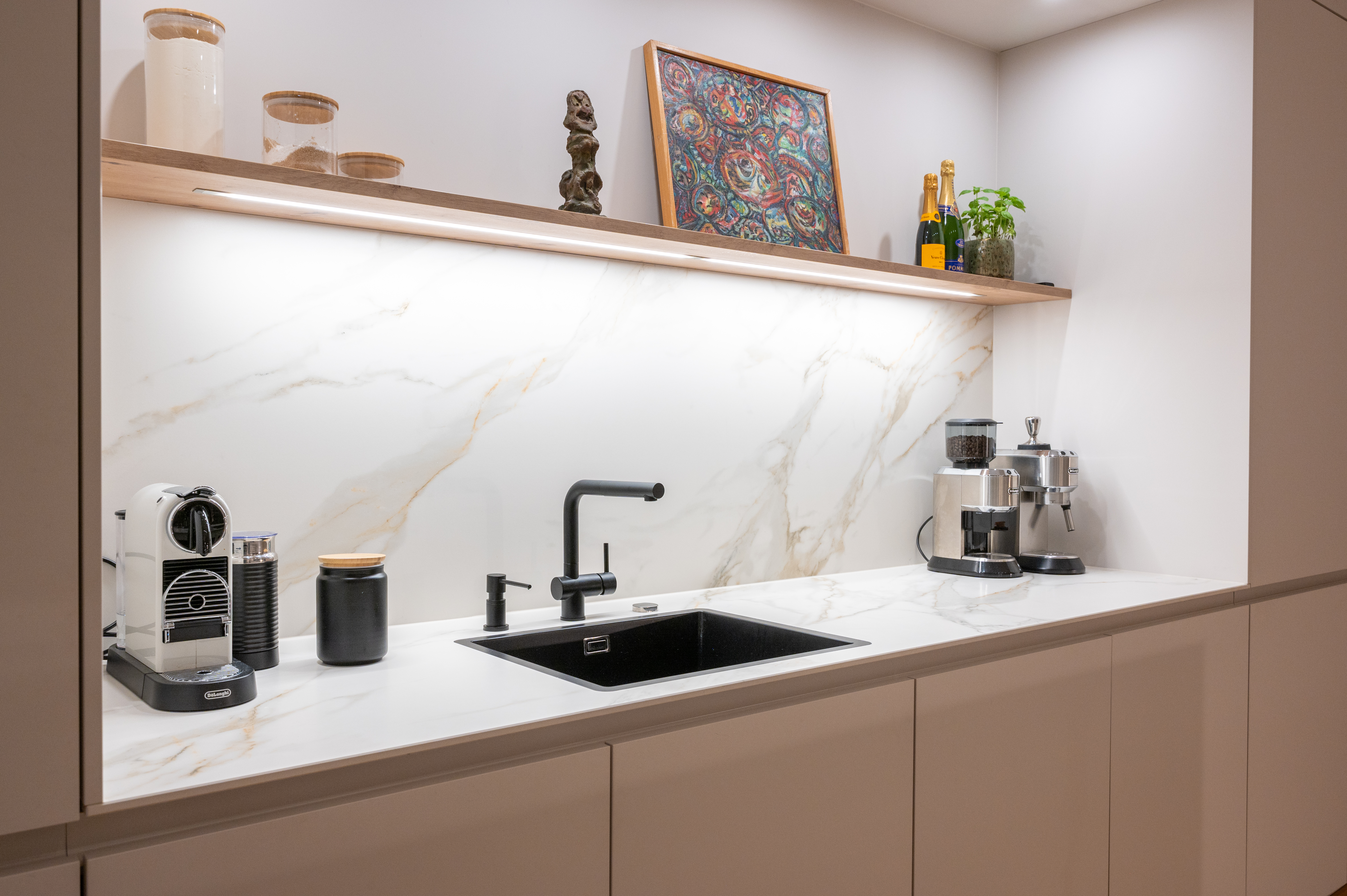 Weiße moderne Küchenzeile mit Marmor-Rückwand, schwarzem Spülbecken und Kaffeemaschinen