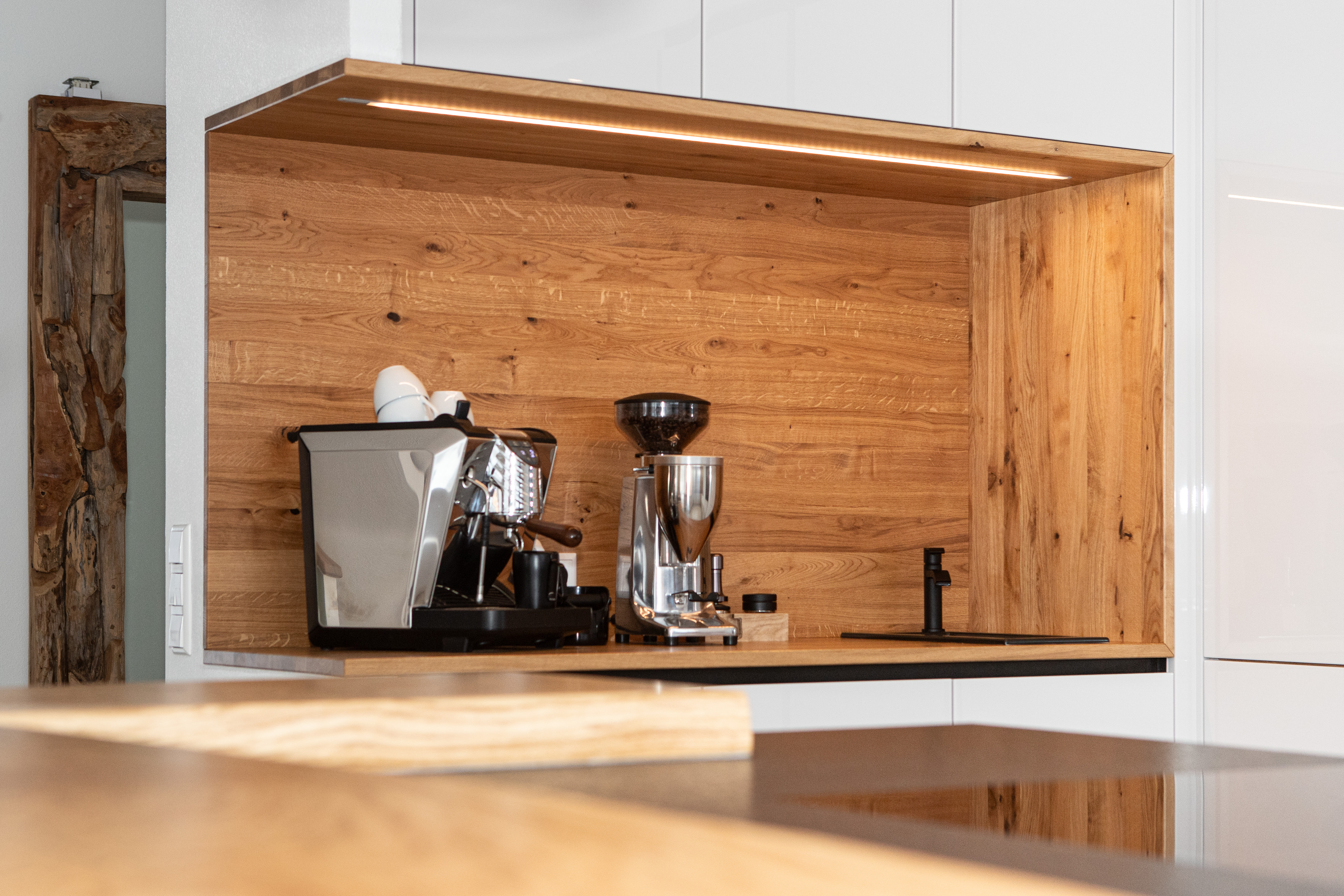 Moderne Küche mit integrierter Kaffeemaschine, Kaffeemühle und Holzverkleidung, stilvoll beleuchtet mit LED-Leiste.