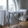 Wäscheständer mit weit auseinander gehängter Wäsche steht längs zu einem hellen Wohnungsfenster, Wäsche in der Wohnung trocknen