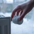 Hand dreht Heizkörperthermostat auf das Schneeflockensymbol der Frostschutzstellung, bevor man die Wohnung im Winter verlässt